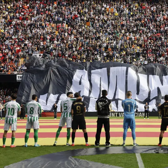 Jugadores del Valencia y Betis frente al tifo desplegado en Mestalla recordando a los municipios afectados por la DANA