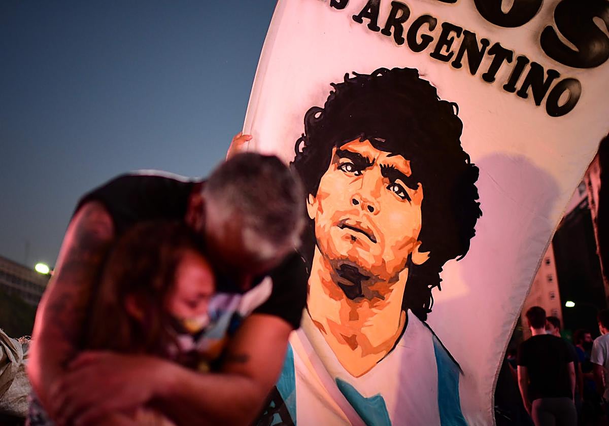 Un padre y su hija se abrazan ante la imagen de Maradona, durante homenaje popular en Buenos Aires, noviembre 2020