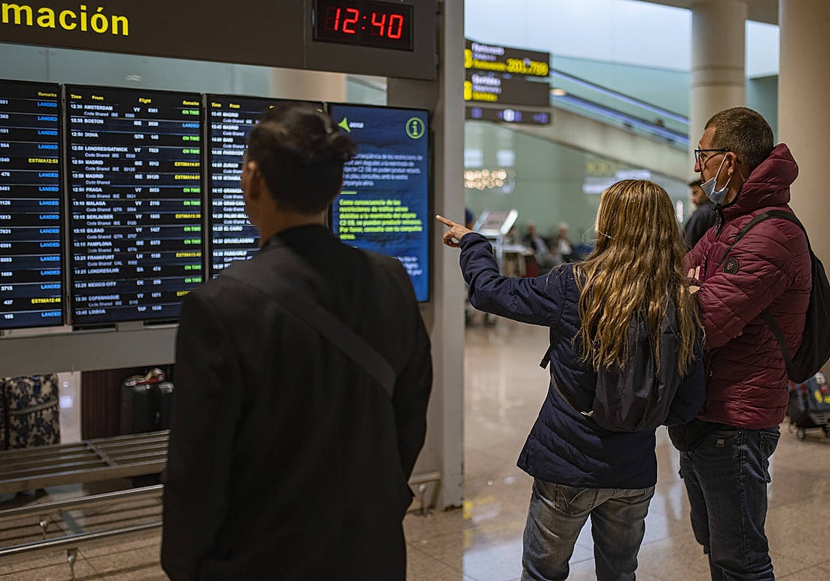 Varias personas observan un panel de llegadas en el aeropuerto de Barcelona