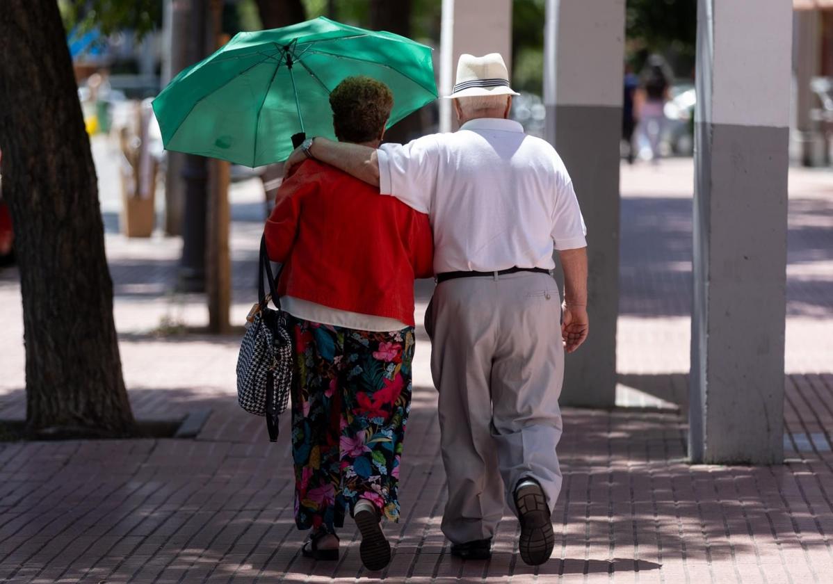 Dos personas mayores caminan bajo la sombra de un árbol, en Madrid