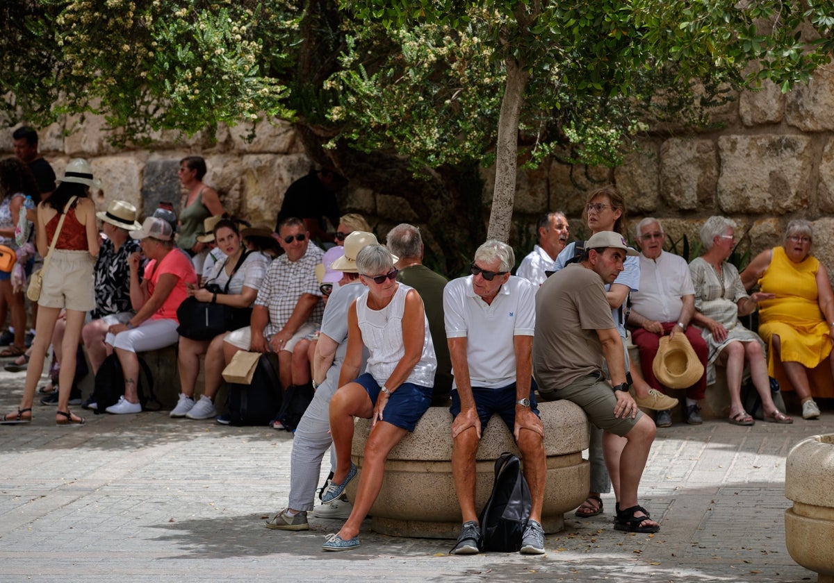 Unos turistas descansan sentados a la sombra junto a los Reales Alcázares de Sevilla