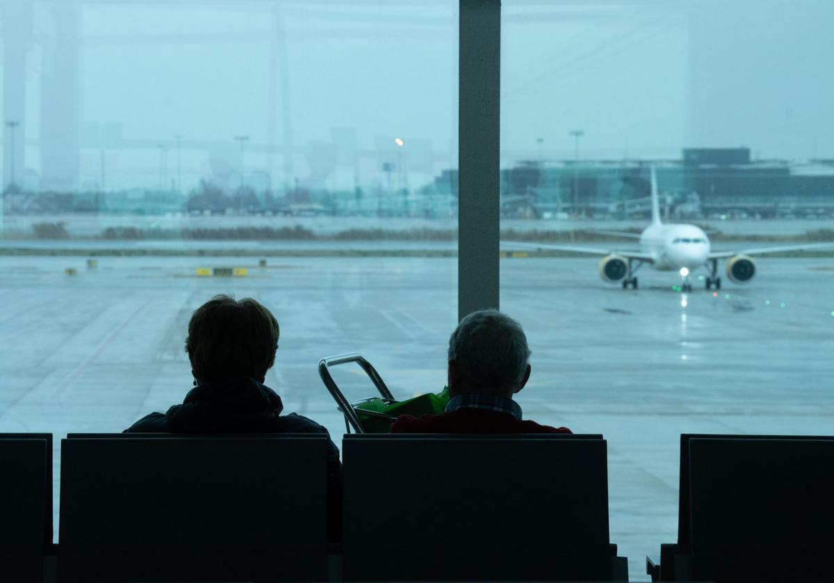 Dos personas esperan sentadas frente a un avión aparcado en la pista del aeropuerto de El Prat, a 19 de enero de 2023