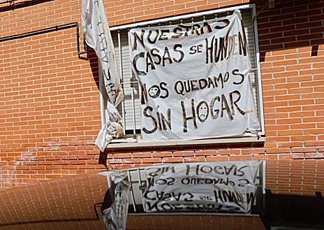 Imagen secundaria 1 - El solar del edificio demolido, cubierto por cemento; pancartas pidiendo soluciones, y grietas en algunos de los edificios