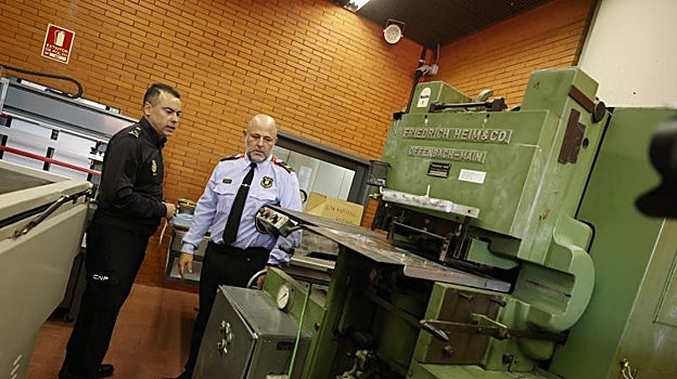 Un agente de la Policía Nacional y uno de los Mossos d'Esquadra junto a una de las maquinas para falsificar billetes
