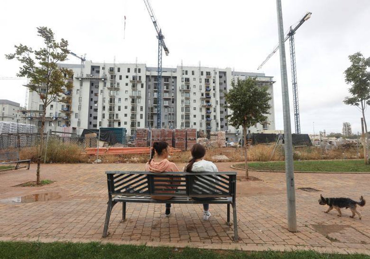 Dos jóvenes sentadas en un banco observan una promoción de nueva construcción en Fuente de la Salud