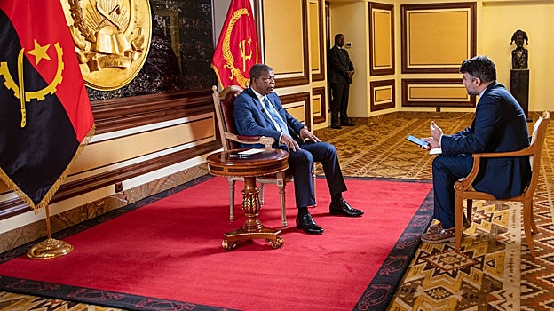 Las banderas de Angola y del Palacio Presidencial presiden el escenario de la entrevista junto a un gran escudo de oro