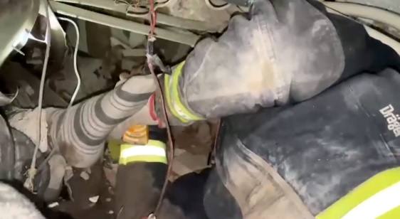 Uno de los bomberos dando de beber a la niña, de la que solo asoma un pie bajo los escombros