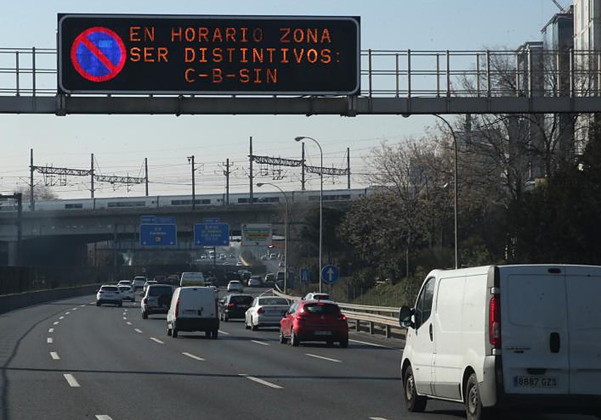 Varios turismos circulan por Madrid bajo un cartel de prohibición de aparcamiento a los coches más contaminantes