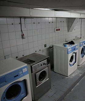 Imagen secundaria 2 - Ventanas tapiadas con ladrillos y otras con cristales rotos; e interior del colegio mayor (fotos de 2014) con imágenes de los baños y lavadoras en el momento del cierre