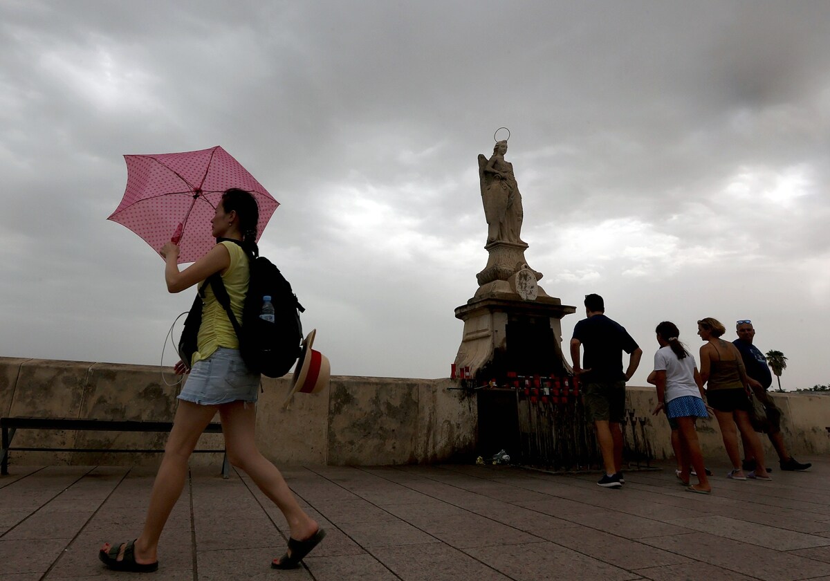 Nubes en el  entorno del Puente Romano de Córdoba y una joven abriendo un paraguas