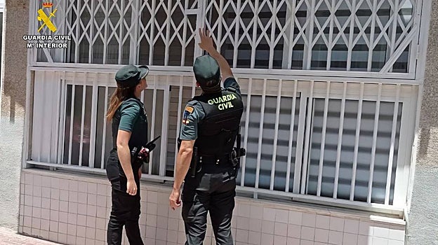 Dos guardias civiles tratan de ubicar la parte de la reja que deben forzar para acceder a la vivienda