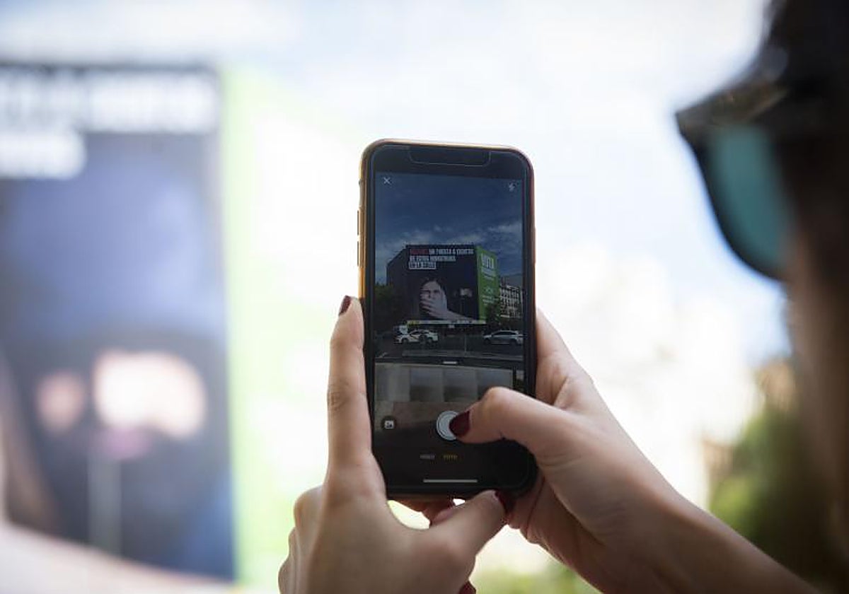 Una ciudadana hace una foto con su teléfono a la lona con propaganda electoral colgada por Vox en Madrid