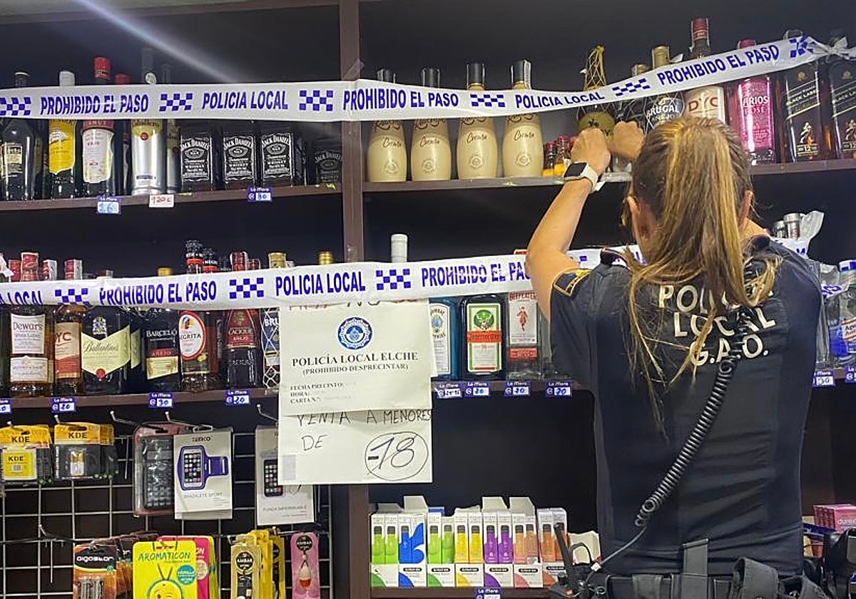 Una policía local de Elche precinta botellas de alcohol en venta irregularmente a menores de edad.