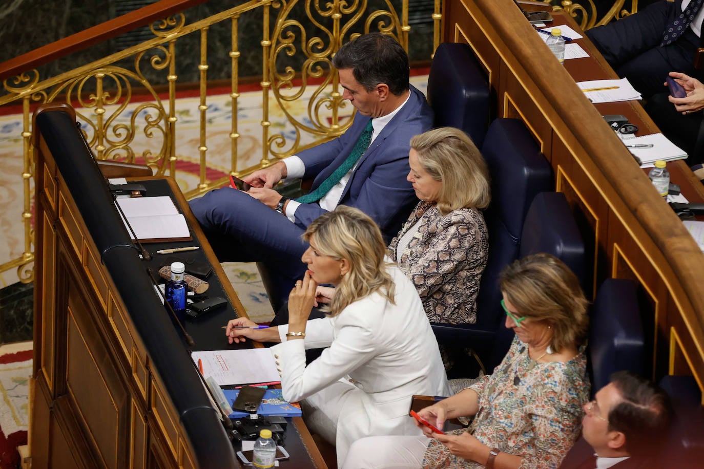 El presidente del Gobierno en funciones, Pedro Sánchez, junto a sus vicepresidentas en funciones Nadia Calviño y Teresa Ribera revisan el móvil mientras habla el líder del PP Alberto Núñez Feijóo; la vicepresidenta segunda Yolanda Díaz sigue atenta el discurso