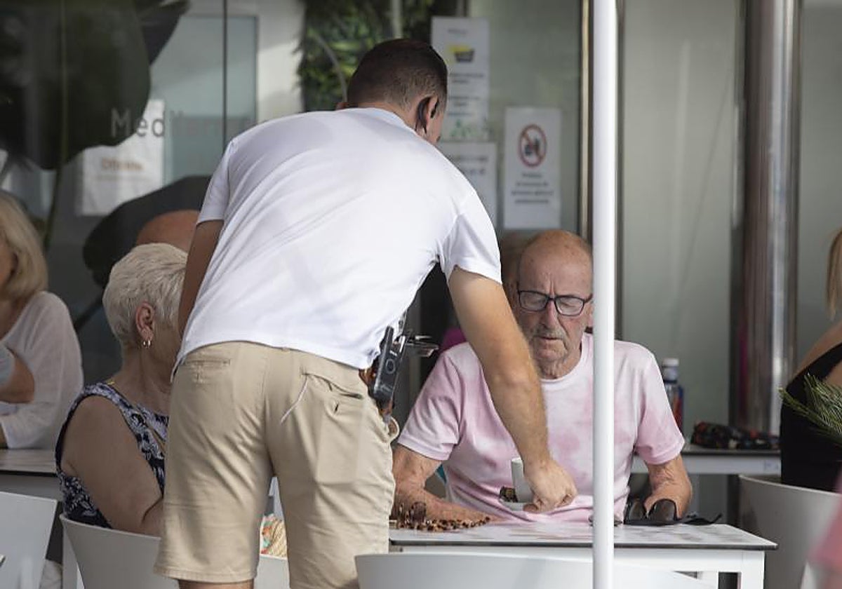 Imagen de archivo de un bar en el que un camarero atiende a dos clientes.