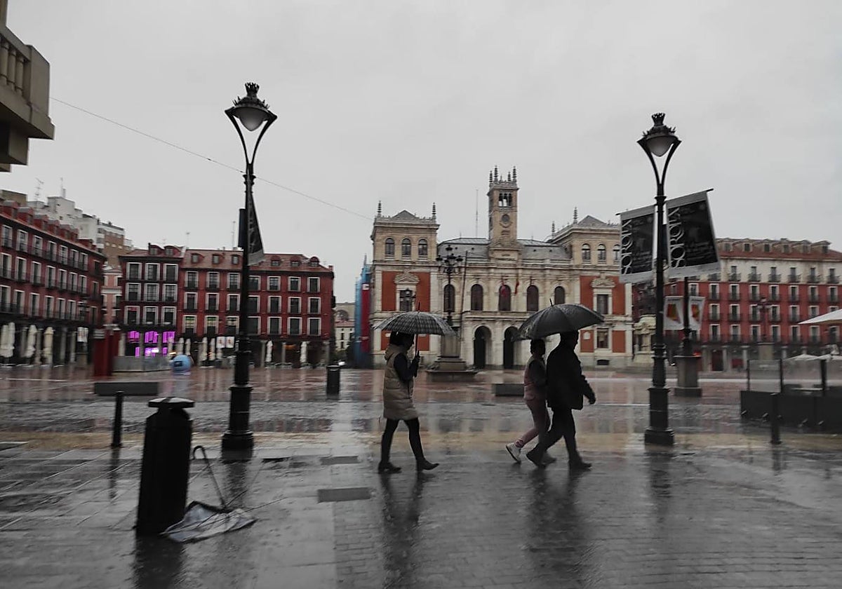 Varias personas, por la Plaza Mayor de Valladolid, este domingo por la tarde provistas de paraguas para la lluvia
