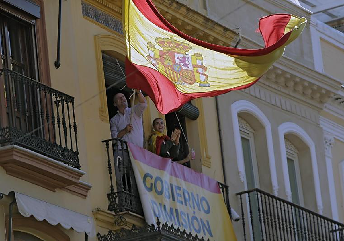 En la plaza de San Francisco de Sevilla, varias personas se asoma al balcón del que cuelga una pancarta con el lema «Gobierno, dimisión»