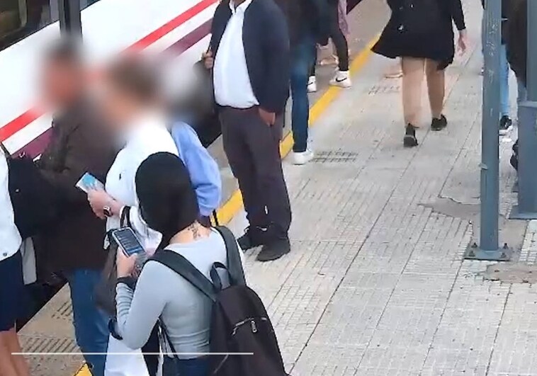 Uno de los ladrones, con chaqueta oscura a la izquierda, roba el teléfono de la mochila de un viajero