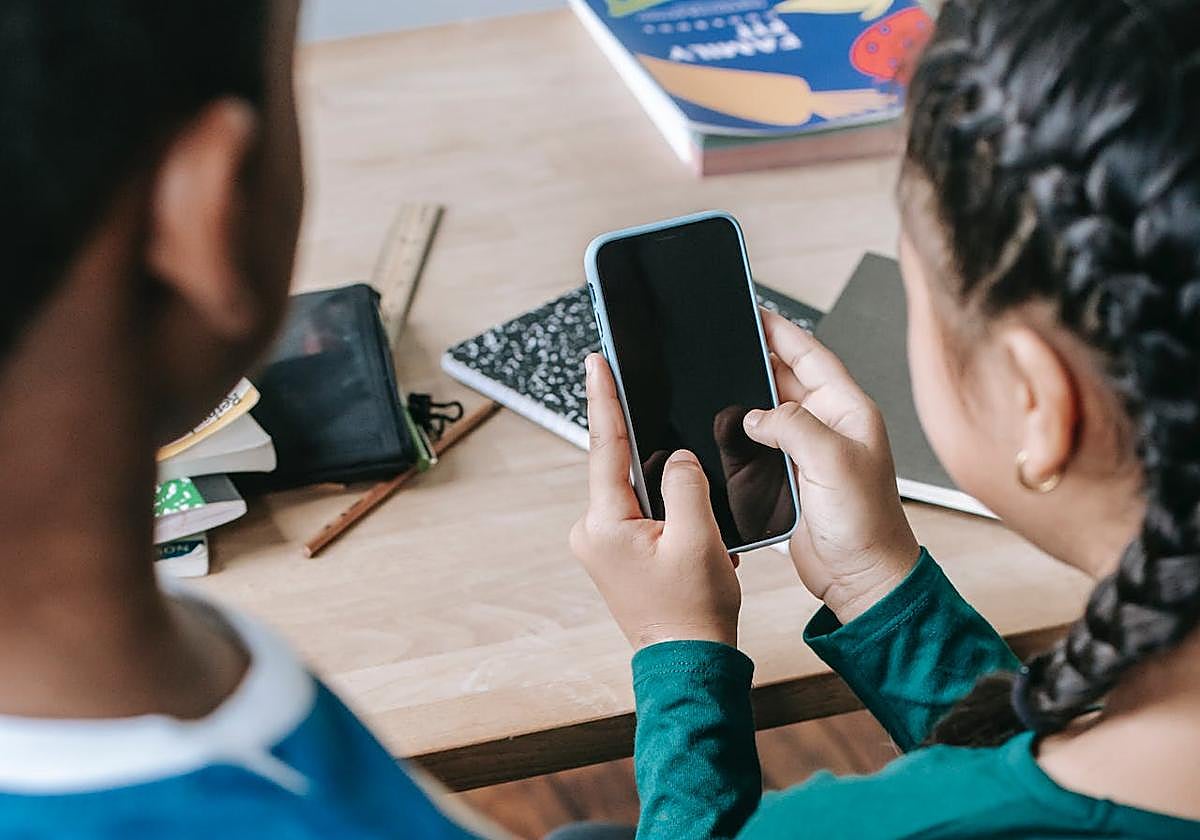 Dos niños, atentos a un teléfono móvil en un aula