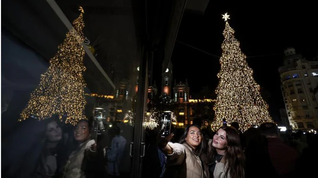 Dos jóvenes se hacen un selfie cerca del árbol de Navidad iluminado.