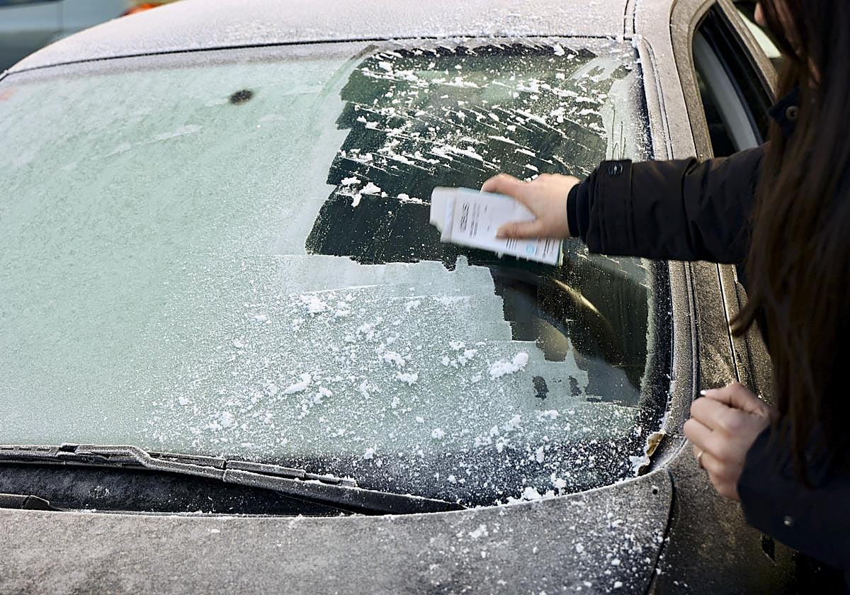 Una mujer retira escarcha del parabrisas de un vehículo