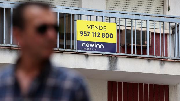 Un hombre pasa delante del cartel de venta de una vivienda en Córdoba