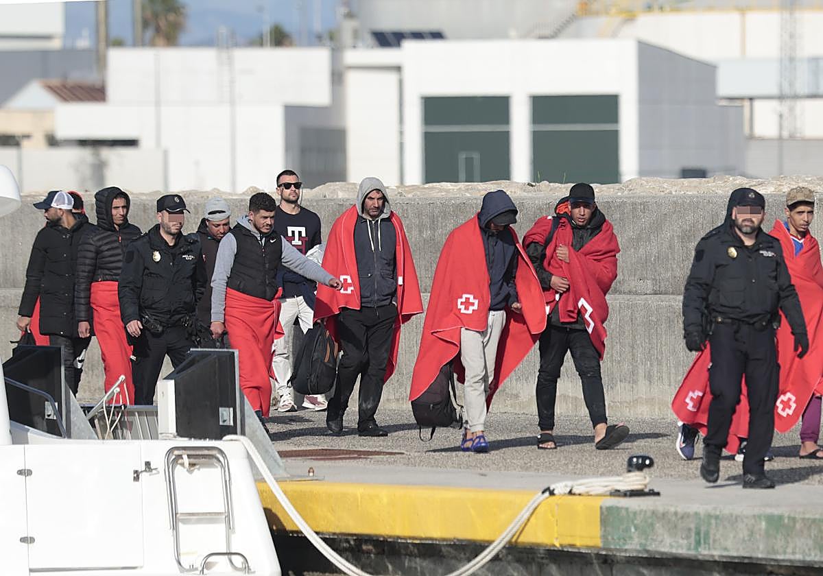 Migrantes llegados a la costa de Cádiz y agentes de la Policía Nacional custodiándolos