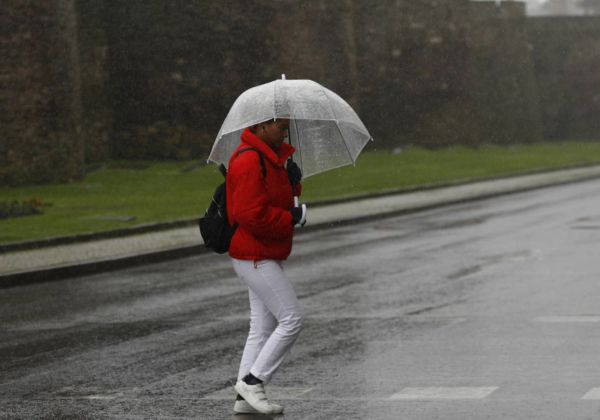 Una persona protegiéndose de la lluvia en un calle de Lugo