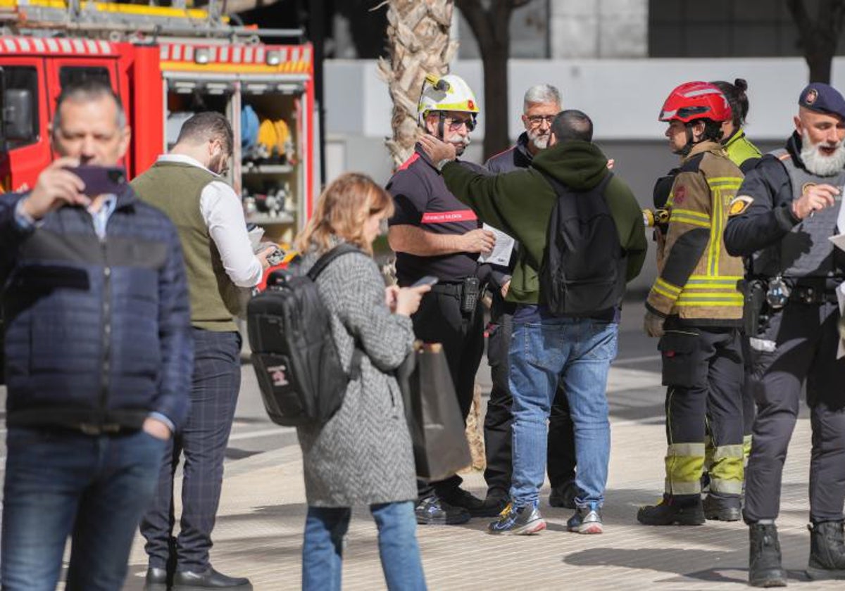 Bomberos con algunos de los afectados del incendio del edificio, en las inmediaciones del inmueble, en el barrio de Campanar