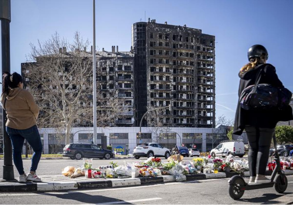 Flores en el suelo en memoria de las víctimas mortales del incendio, con los esqueletos de los edificios del barrio de Campanar al fondo