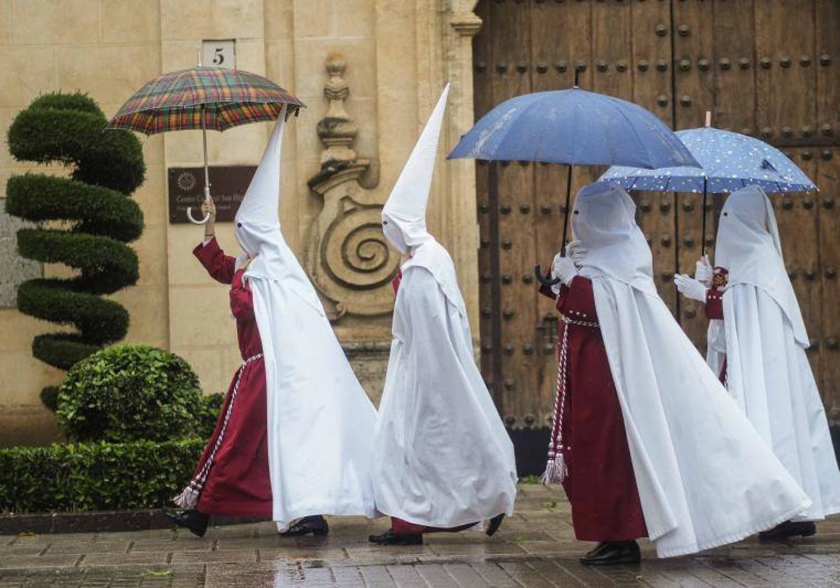 Nazarenos de la Hermandad de La Sentencia se protegen de la lluvia con paraguas