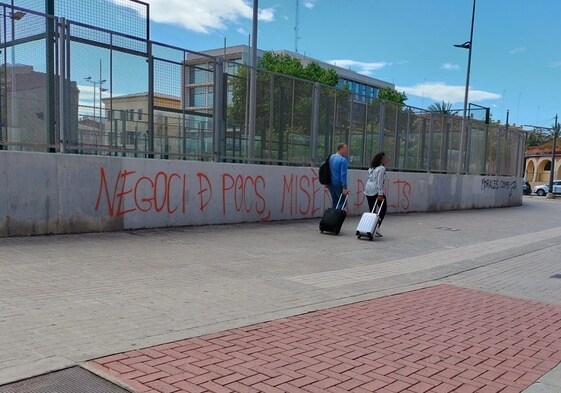 Imagen de dos turistas en el barrio del Cabanyal, en Valencia. De fondo, una pintada en la que se puede leer: 'Negocio de pocos, miseria de muchos'