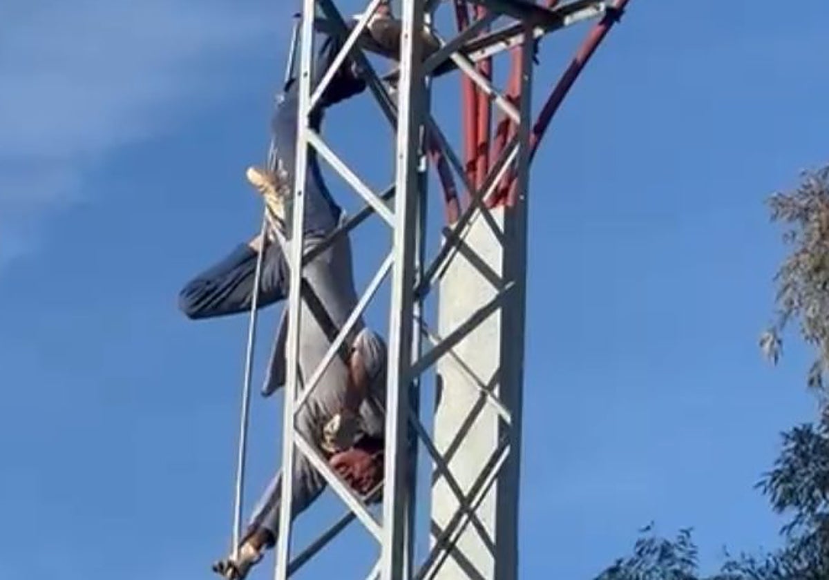 Un hombre suspendido boca abajo enganchado en una torre de luz