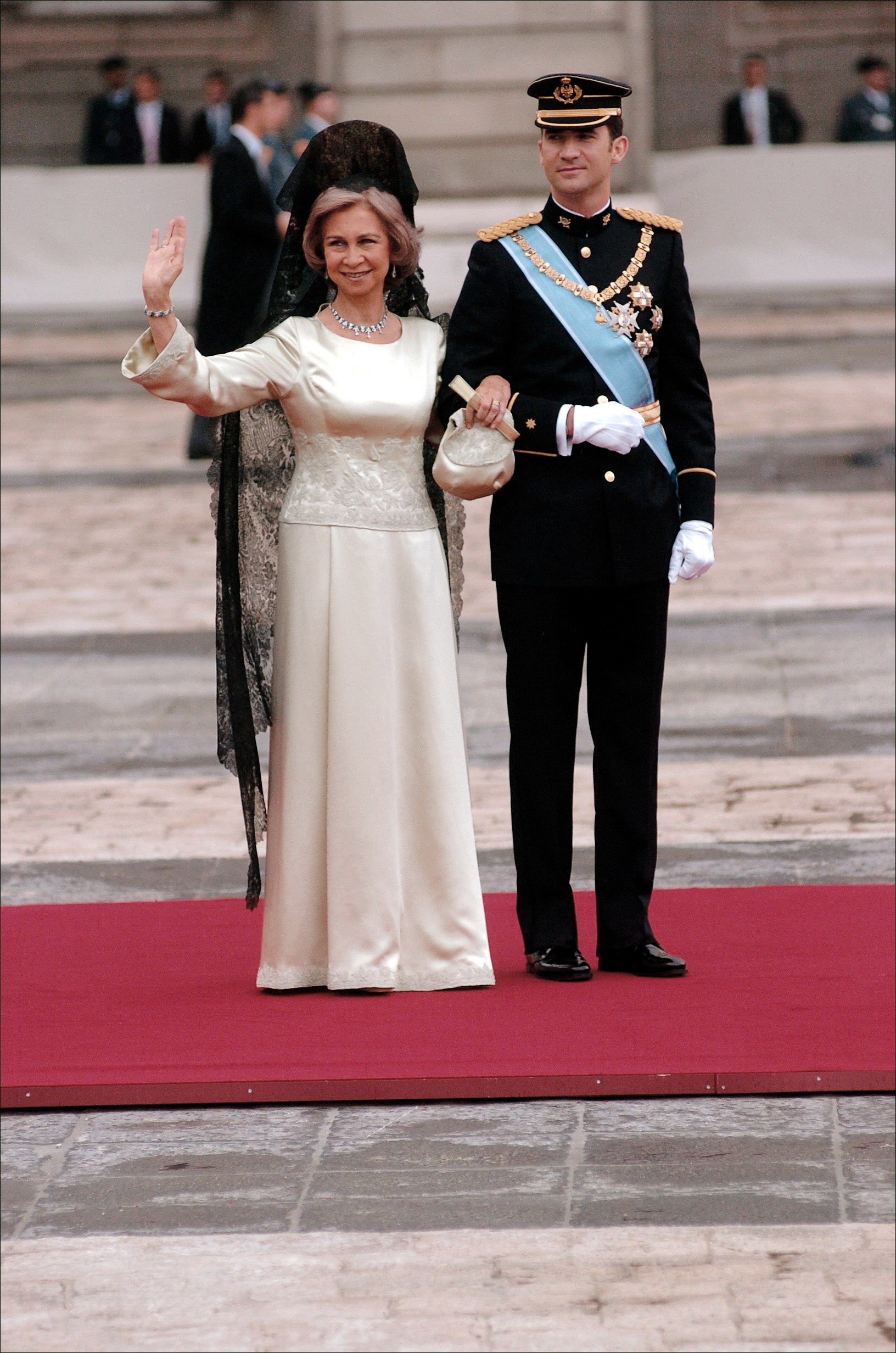Cerrados los paraguas y sin lluvia, Don Felipe recorría junto a la Reina Sofía la plaza de la Armería. Unos 200 metros separan la puerta del Palacio Real de la catedral de la Almudena. La madrina escogió un vestido satinado de color champagne con detalles bordados. Fue una creación de Margarita Nuez, una de las diseñadoras habituales y de mayor confianza de la madre del Rey. Como complemento, lució, además de la protocolaria y clásica mantilla española —de encaje de seda oscura, se trata de un regalo que la Reina Sofía recibió en 1994 del Concello de Camariñas (La Coruña)— y peineta, un collar de 20 esmeraldas y diamantes del que cuelgan otros brillantes en forma de lágrima. A juego usó unos pendientes de hilo y lazo de diamantes con esmeraldas. El aderezo fue un regalo que recibió cuando Don Juan Carlos llegó al trono en 1975. Doña Sofía fue la única persona que vistió de largo en la boda real. 