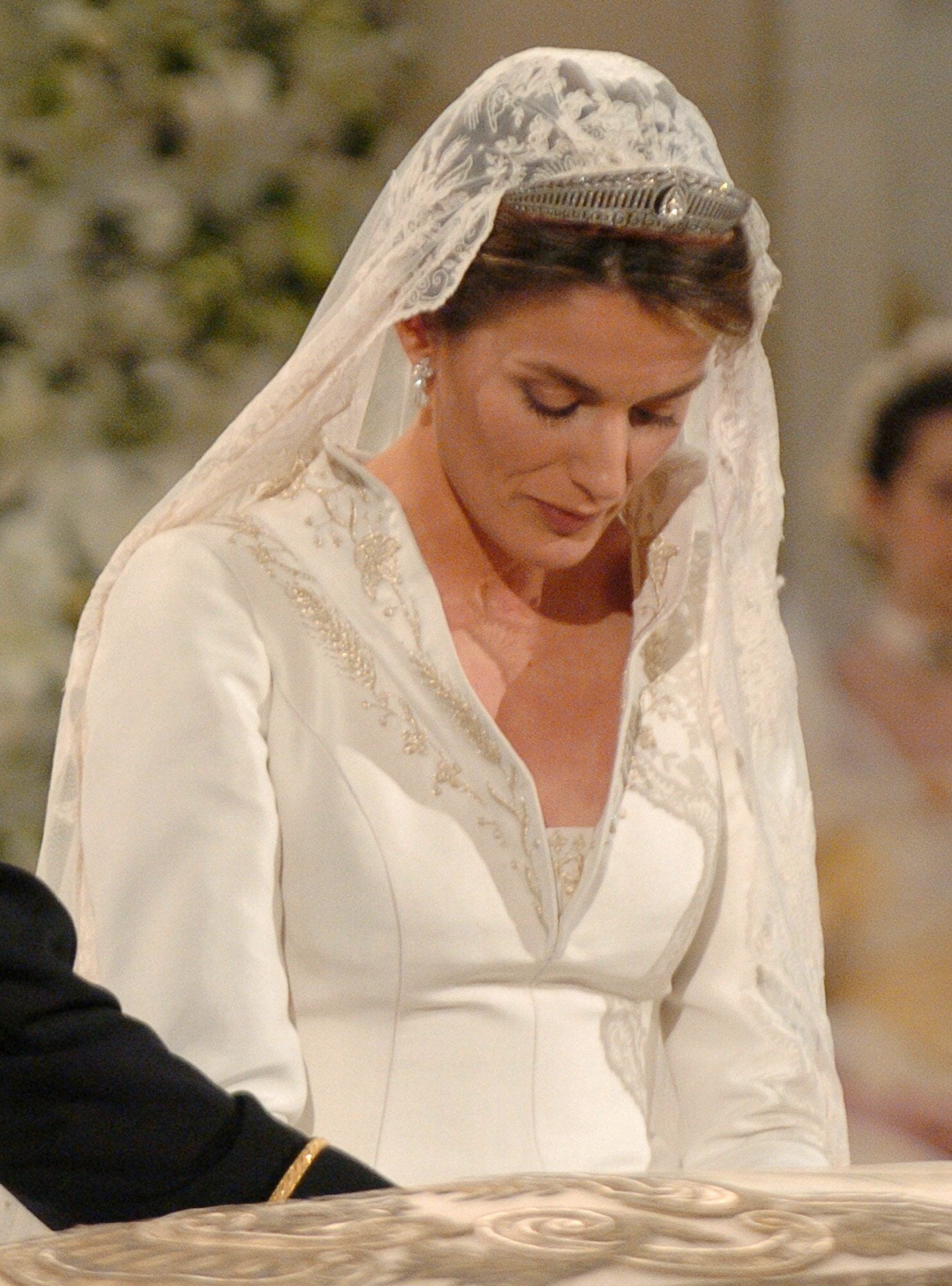 Esta fue una de las primeras imágenes de Doña Letizia convertida oficialmente en Princesa de Asturias. En ella, se puede observar la tiara que lució en la ceremonia nupcial. Fue la joya más comentada del enlace. Se trata de la diadema prusiana de estilo helénico con greca en la base que elaboró el joyero alemán Kosh. Compuesta con hojas de laurel y engarzada en diamantes, fue un regalo del Kaiser Guillermo II a su hija Victoria Luisa de Prusia, abuela materna de Doña Sofía, por su unión con el Príncipe heredero de la Casa de Hannover. La Reina Sofía heredó esta tiara de su madre Federica de Hannover y quiso que Doña Letizia la luciera aquel día. Con ella sujetó la mantilla, con símbolos bordados como la flor de lis, que forma parte del emblema de la Casa de Borbón. En la imagen se pueden observar también los sencillos pendientes de diamantes que lució, que anteriormente perteneció a la Condesa de Barcelona y que, se dice, fue un regalo de los Reyes.