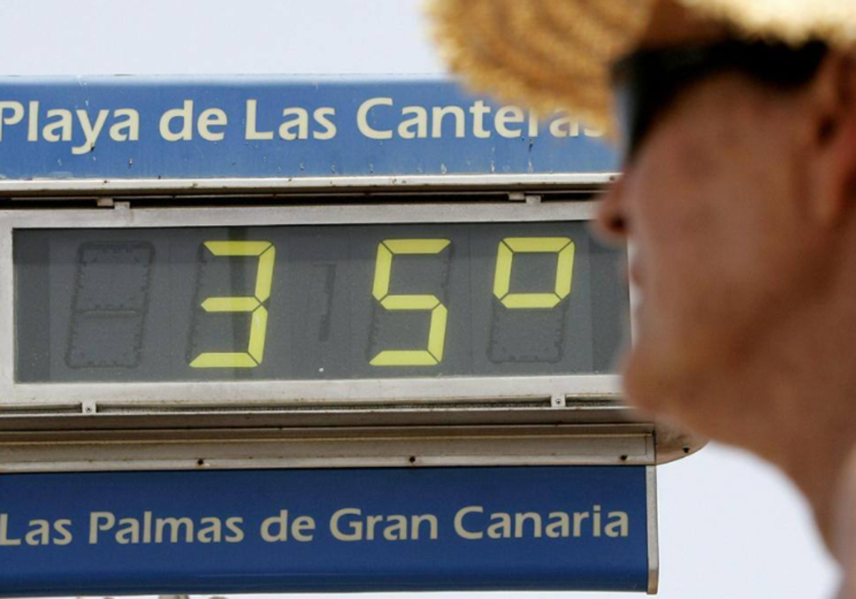 Una mujer se protege del calor junto a uno de los termómetros de la playa de Las Canteras, en Gran Canaria