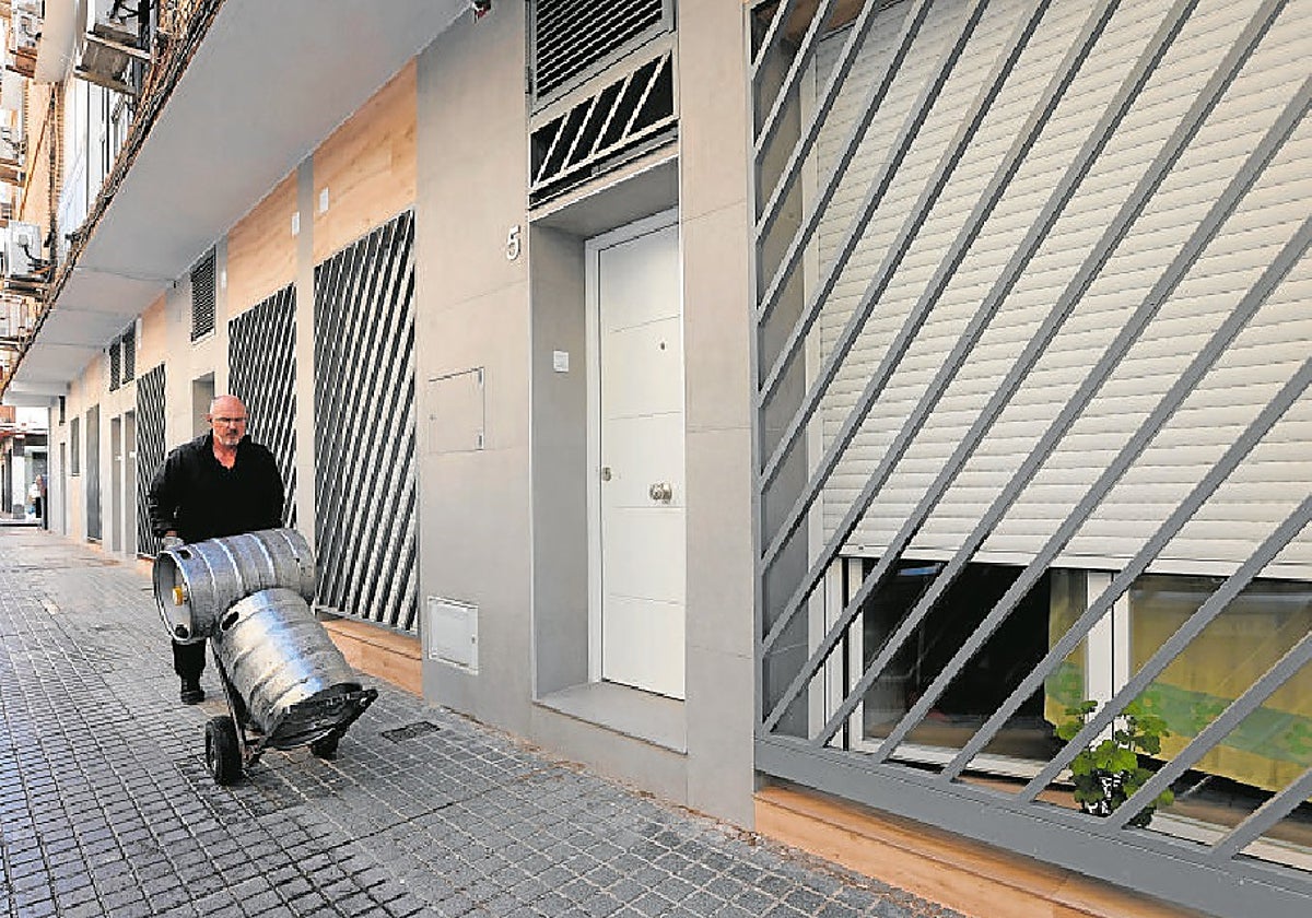 Un hombre transporta unos barriles junto a una vivienda turística