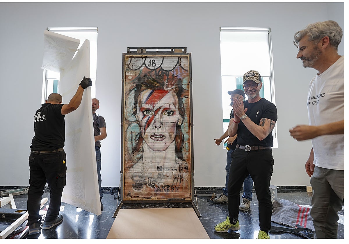 El artista Jesús Arrúe (2º d), asiste a la instalación del grafiti de David Bowie, obra procedente del Centre del Carme Cultura Contemporània, en la exposición permanente del L'ETNO
