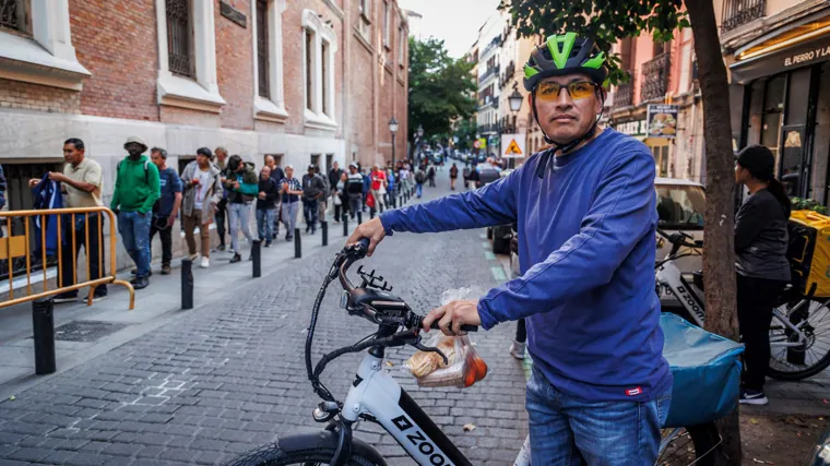 Osman posa con su ración de comida, junto a la cola que se forma a las puertas de la Real Hermandad del Refugio