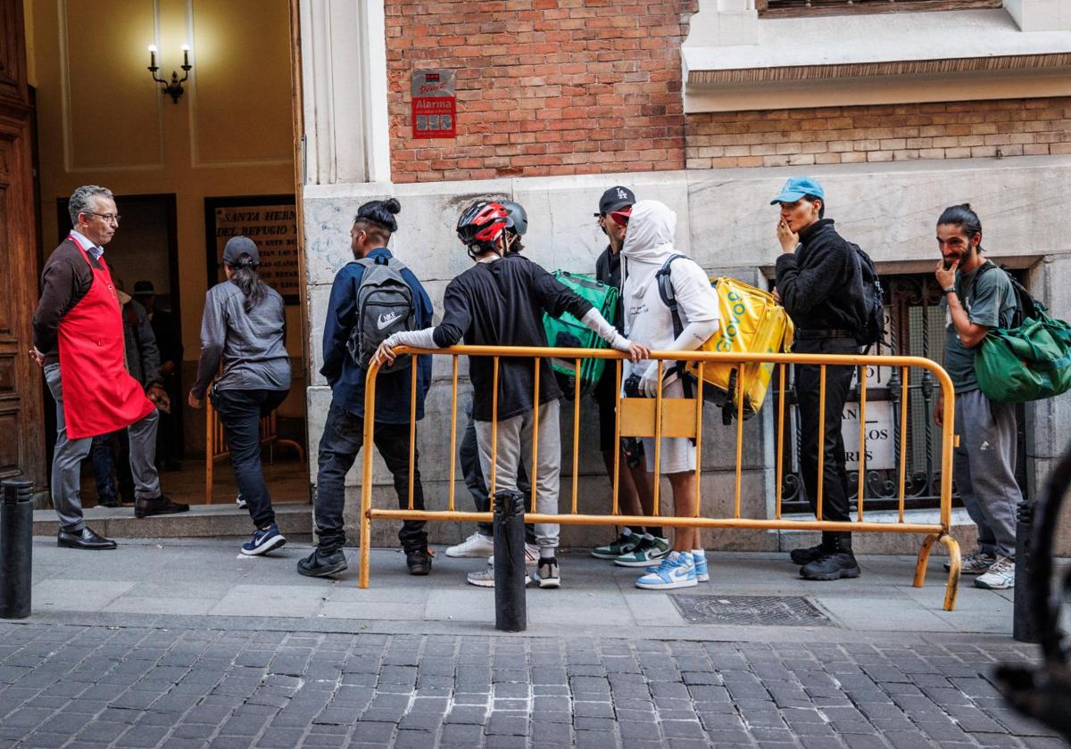 Varios 'rider' se ponen a la cola en el comedor social de la Parroquia Real Hermandad del Refugio, en Malasaña