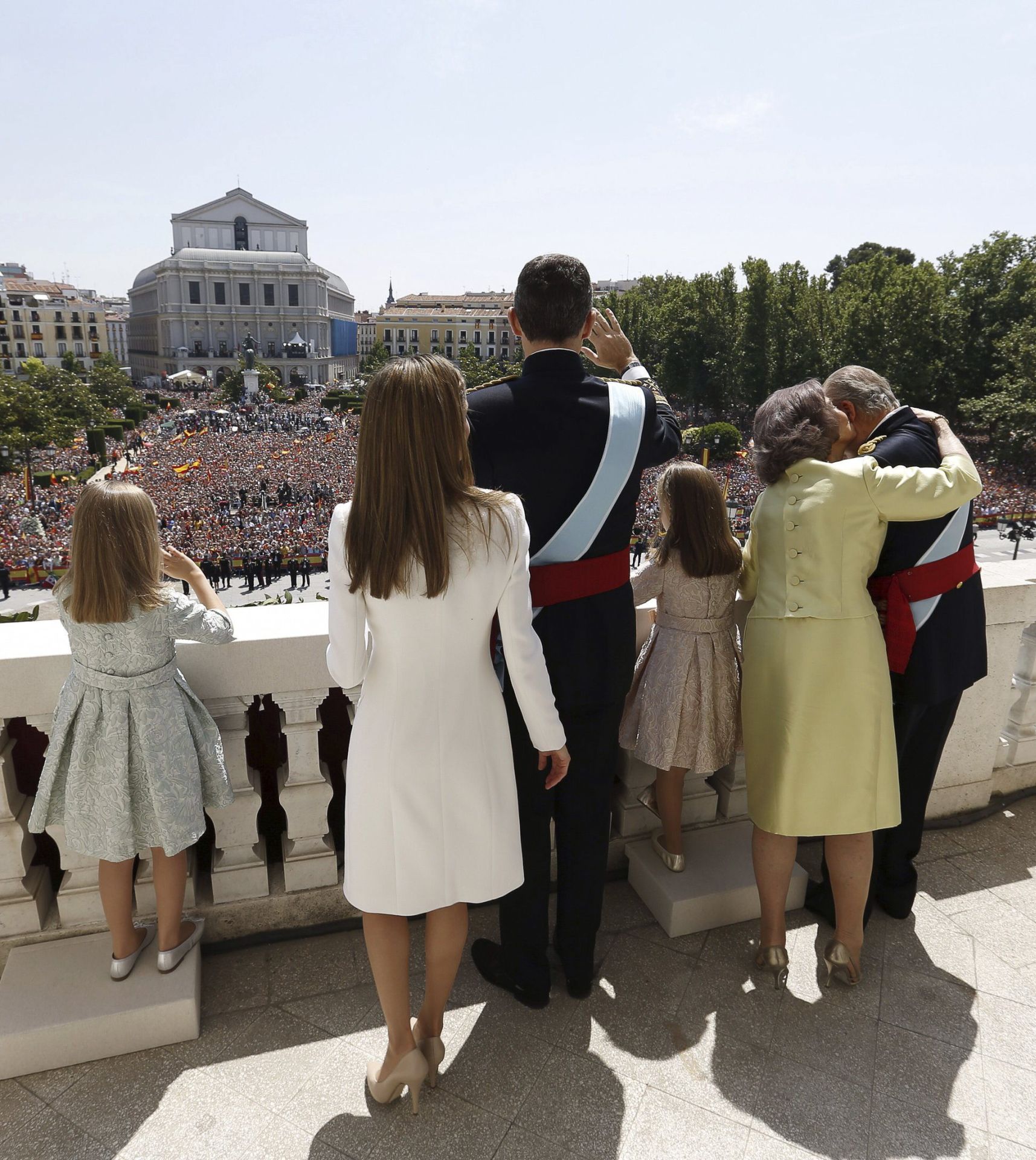 Los Reyes, Don Felipe y Doña Letizia, junto a sus hijas, la Princesa Leonor y la Infanta Sofía, y Don Juan Carlos y Doña Sofía, saludaron desde el balcón central del Palacio Real a los ciudadanos que se congregaron en la Plaza de Oriente para rendir homenaje a los nuevos monarcas. En esta imagen se puede apreciar los pequeños escalones que las menores poseían para poder ver con claridad. Además, se observa la muestra de cariño de la Reina Sofía hacia el Rey Juan Carlos.