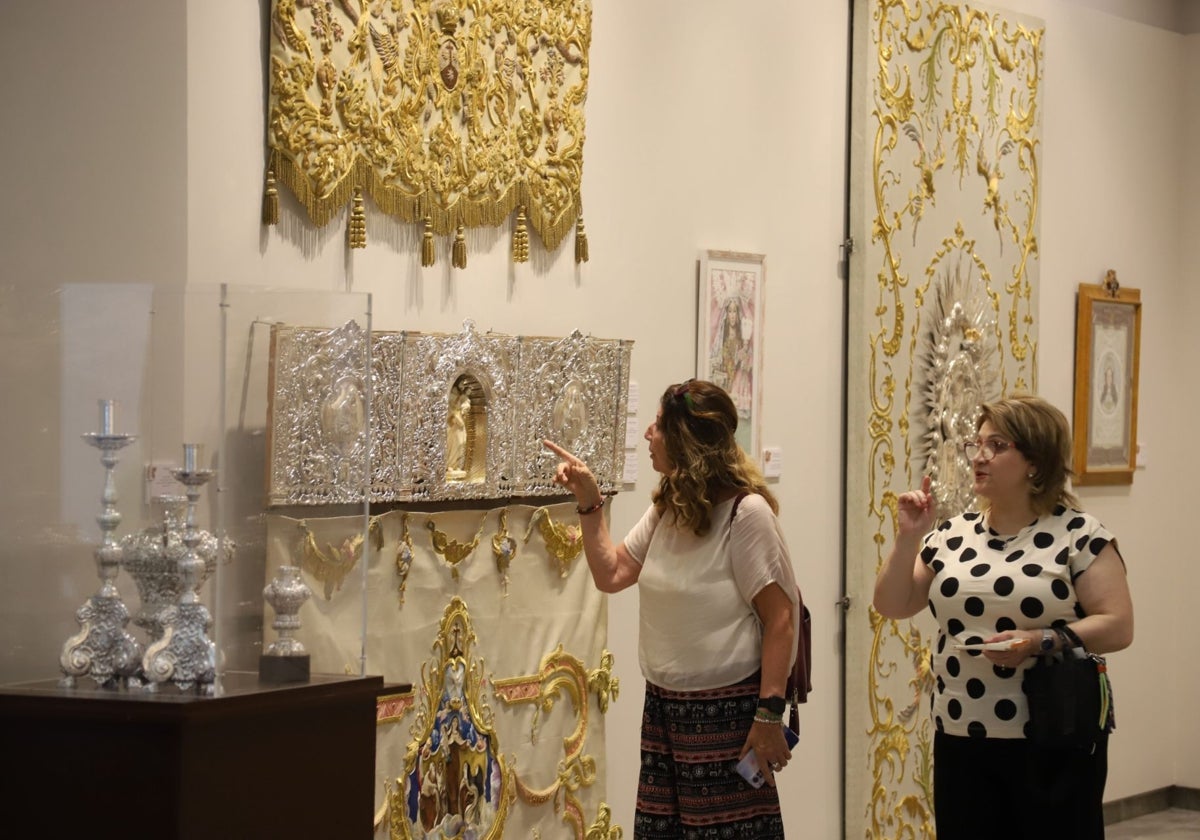 Dos mujeres admiran el respiradero del palio de la Virgen del Carmen de San Cayetano, en la exposición en la Fundación Caja Rural del Sur