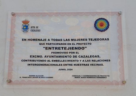 Imagen secundaria 1 - La iniciativa es del Ayuntamiento de Cazalegas, que ha homenajeado a unas 100 mujeres, de entre 7 y 102 años, que han colaborado en el proyecto. Arriba, toldo de mandalas en la plaza de la Virgen del Rosario. Sobre estas líneas, placa que se ha colocado en la plaza y un detalle de los productos servidos a las mujeres en la merienda