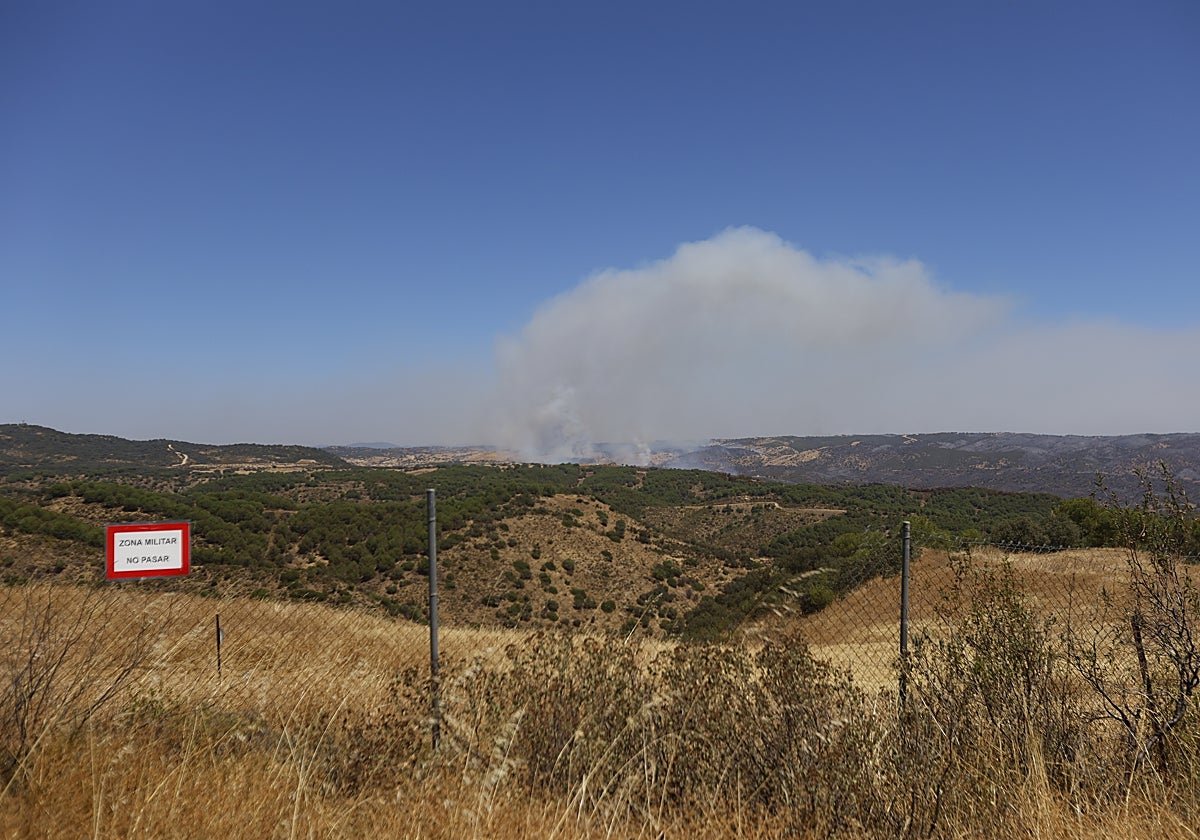 La cortina de humo del incendio vista detrás de la valla de seguridad del campo de maniobras de Cerro Muriano