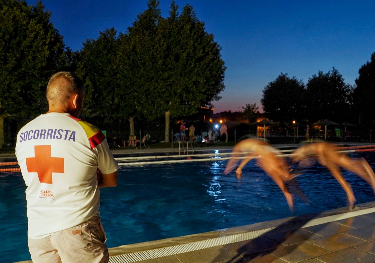 Un socorrista observa a dos nadadores lanzándose a una piscina de noche