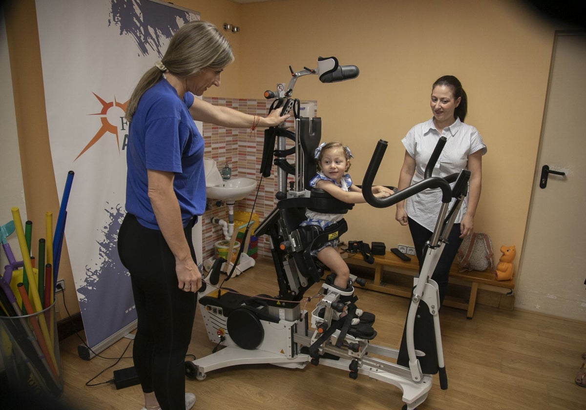 Carmen, en el Innowalk Pediátrico, con la fisioterapeuta y su madre, a la derecha