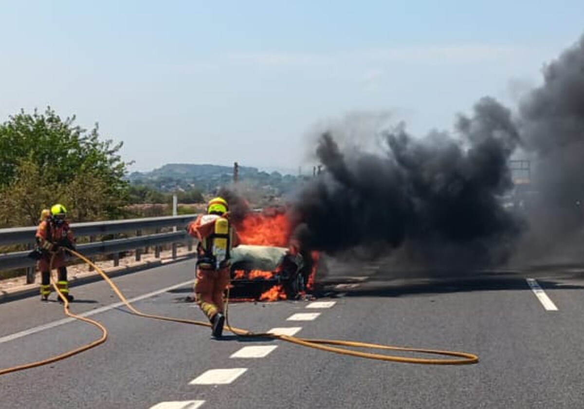 Bomberos trabajan en la extinción del fuego del coche accidentado en la A-3 en Ribarroja (Valencia)