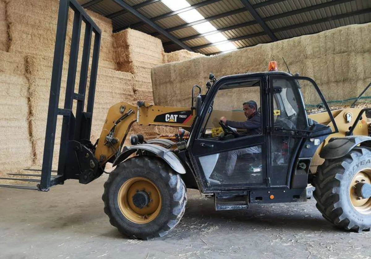 Un trabajador mueve alpacas de paja en una nave de almacén agrícola