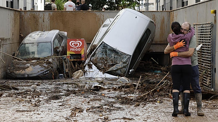 Dos vecinos se abrazan a la entrada de un garaje en Paiporta, Valencia, tras el paso de la DANA