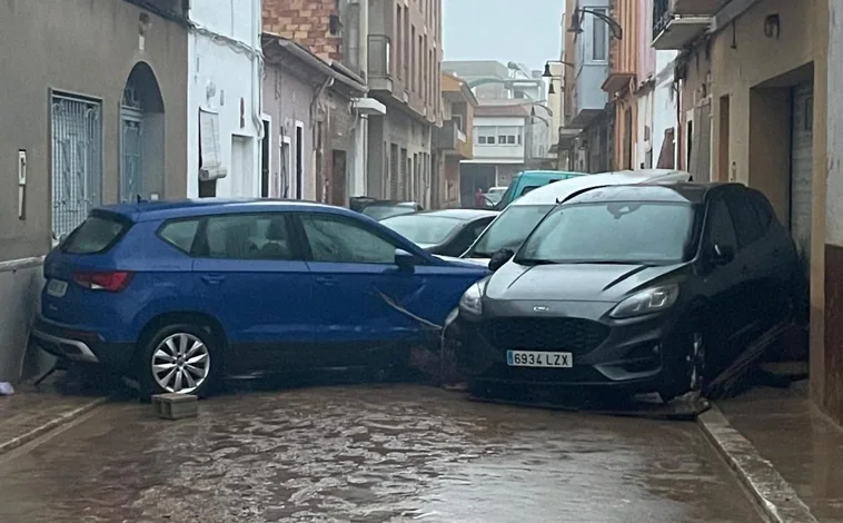 Imagen principal - En la imagen superior, coches amontonados en una calle de Guadassuar. Debajo a la derecha, material enviado por la hermandad del Vía Crucis. A la izquierda, cofrades de Pasión organizando la ropa y demás productos que enviarán pronto  